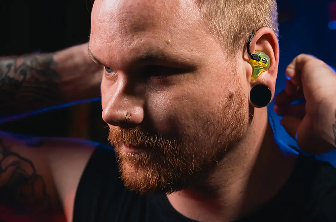 Eine Person mit Tätowierungen setzt gelbe Ohrstöpsel ein, um sich auf eine laute Veranstaltung oder Umgebung vorzubereiten.