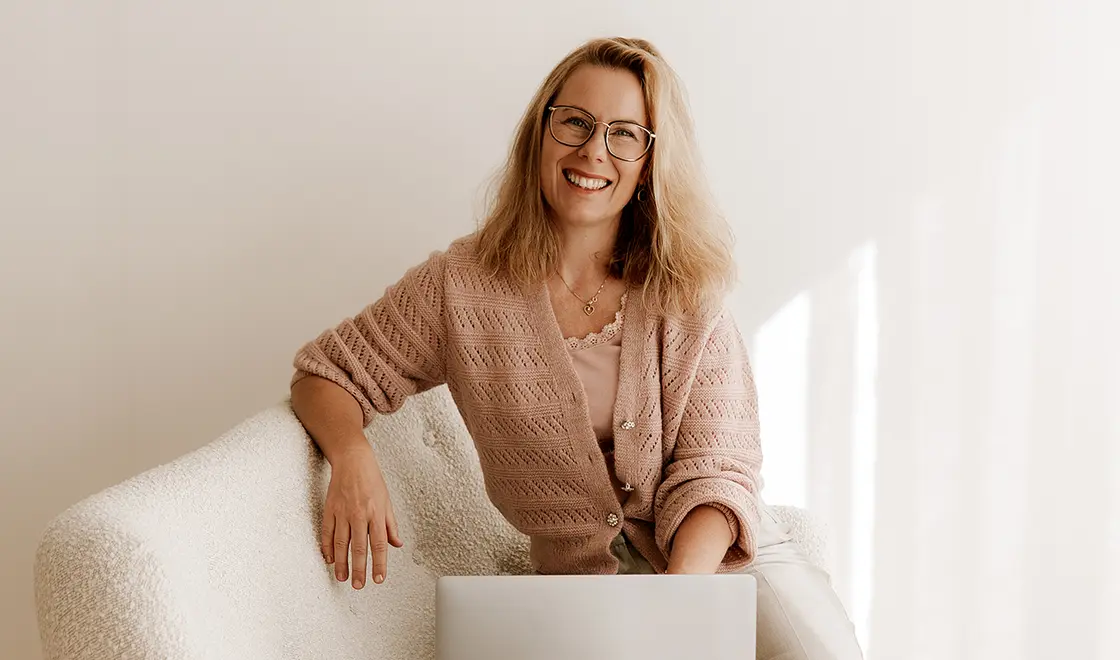 Geschäftsführerin sitzt mit Brille auf einem weißen Sofa und benutzt einen Laptop in einem hellen, minimalistischen Raum.