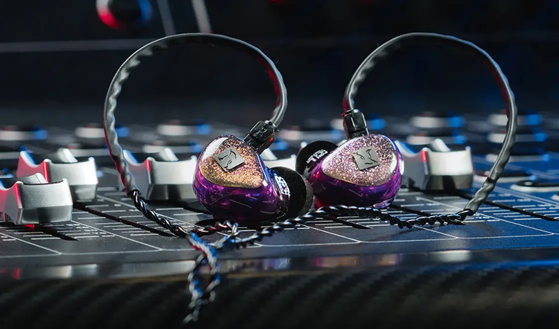 Ein Paar In-Ear-Kopfhörer auf einem Tonmischpult mit bunten Lichtern im Hintergrund.