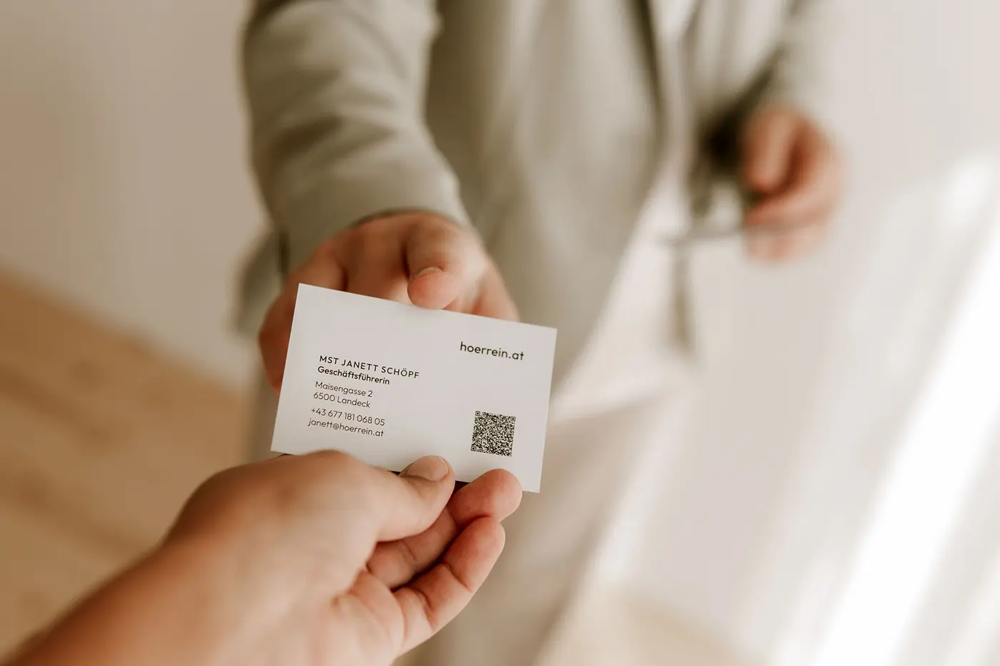 Eine Frau in einem Anzug übergibt die Visitenkarte einer anderen Person.