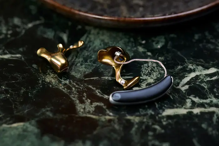 Ein schwarz-goldenes Hörgerät liegt auf einer dunkelgrünen Marmoroberfläche.