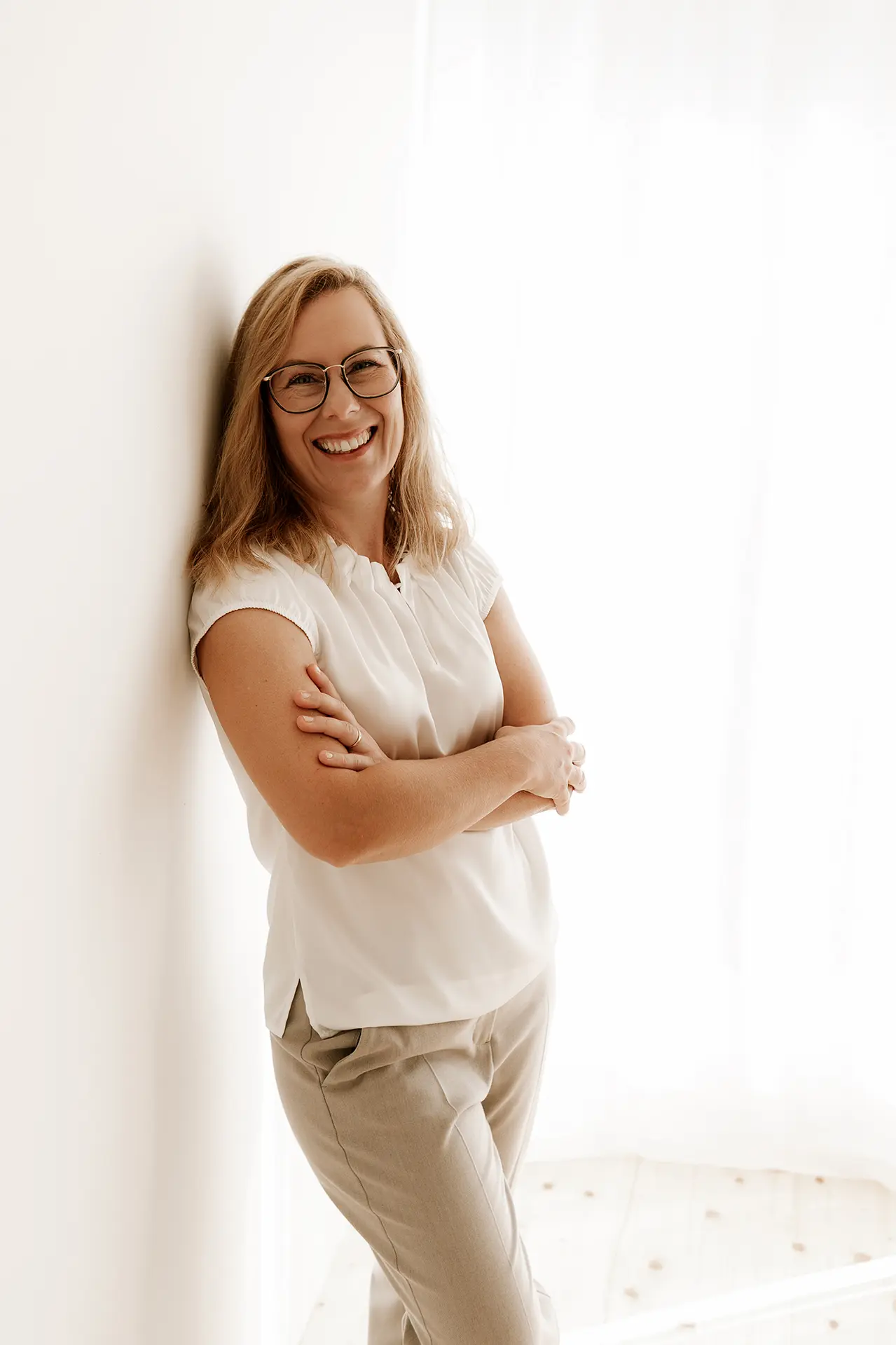 Die Geschäftsführerin Janette steht in einem hellen Anzug vor einer schlichten weißen Wand und schaut lächelnd in die Kamera.