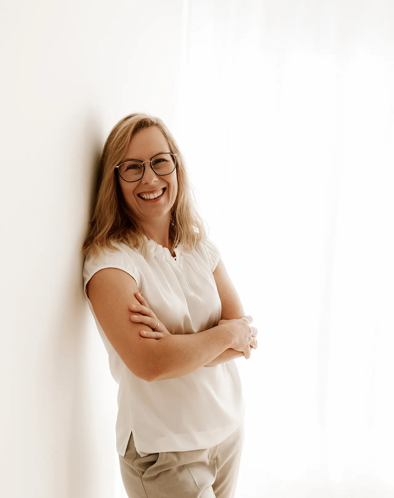 Die Geschäftsführerin Janette steht in einem hellen Anzug vor einer schlichten weißen Wand und schaut lächelnd in die Kamera.