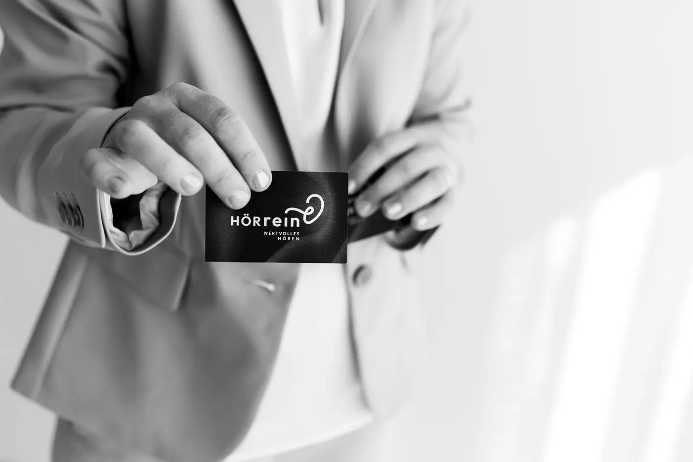 Schwarz-Weiß Foto von der Geschäftsführerin des Unternehmens, wie sie ihre Visitenkarte in die Kamera hält.