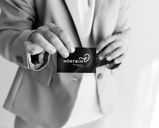 Schwarz-Weiß Foto von der Geschäftsführerin des Unternehmens, wie sie ihre Visitenkarte in die Kamera hält.