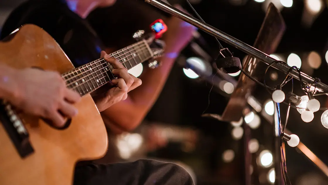 Nahaufnahme einer Person, die eine akustische Gitarre spielt, mit unscharfen Lichtern im Hintergrund.