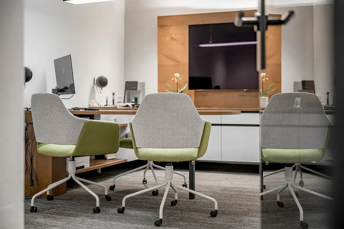 Modernes Büro mit zwei Stühlen, einem Schreibtisch, Computermonitoren, Pflanzen und einem großen, an der Wand befestigten Bildschirm.