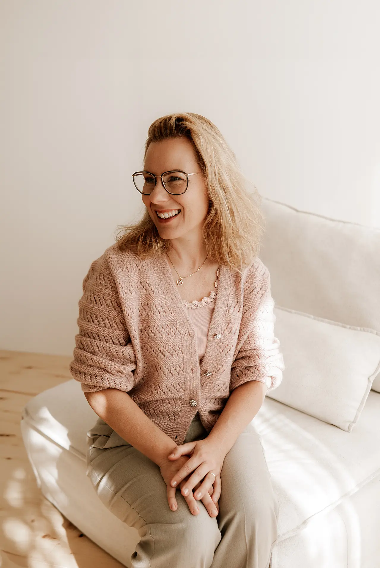 Die Geschäftsführerin Janett sitzt lächelnd auf einer Couch und neigt den Blick leicht ab.