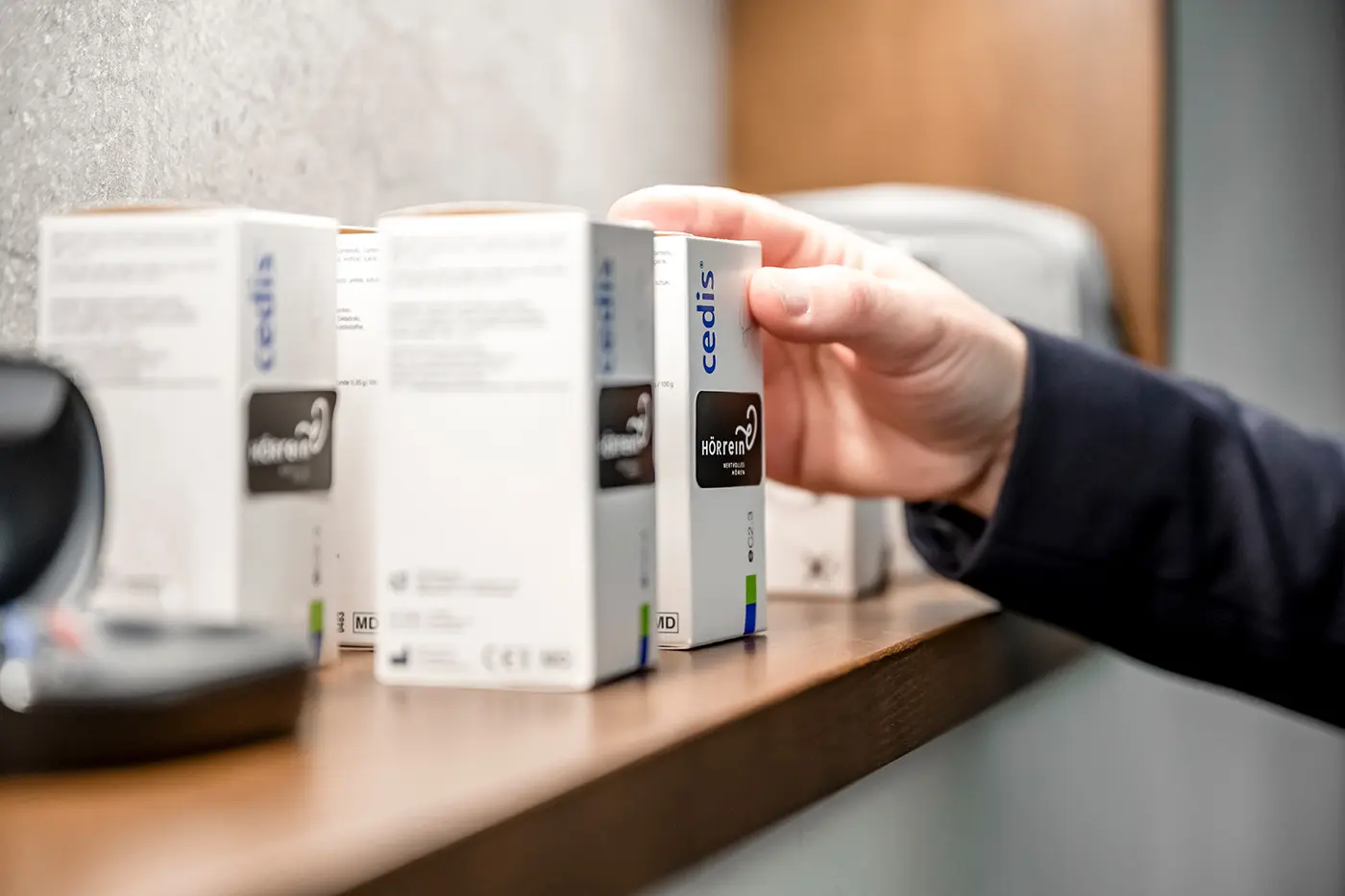 Eine Hand greift nach einer Schachtel inmitten mehrerer weißer Verpackungen, die auf einem Holzregal stehen.