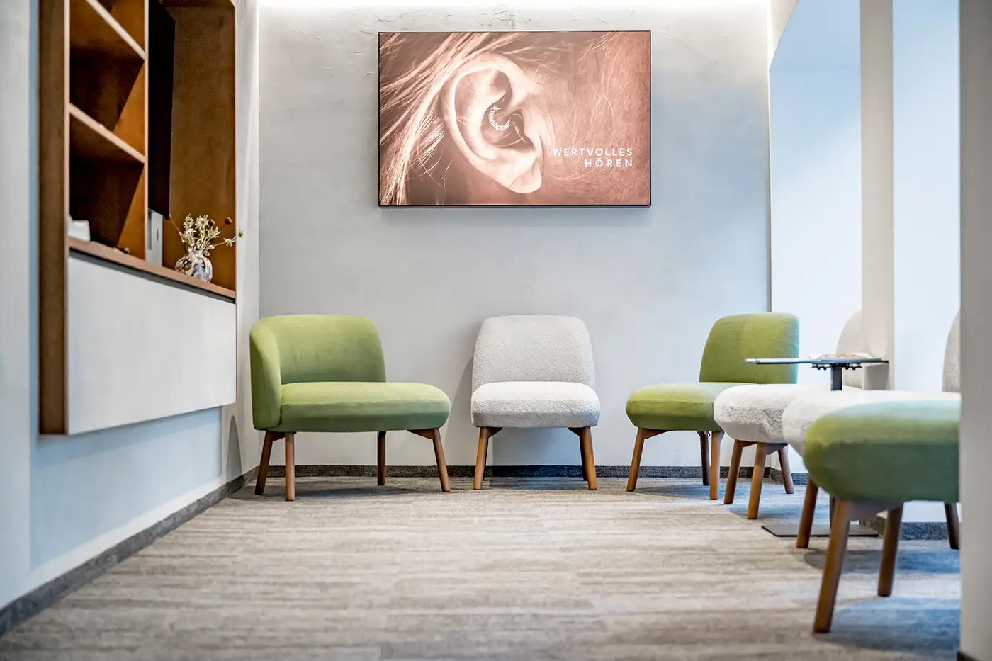 Detailaufnahme des modernes Wartezimmers mit grünen und weißen Stühlen, Teppichboden und eingebauten Holzregalen.