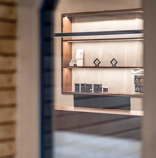 Unscharfer Blick durch ein Fenster auf ein modernes Regal mit Hörsystemen in einem stilvollen Raum.