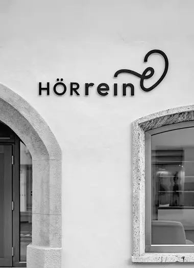 Schwarz weiß Foto der Aussenfassade. HÖRrein Logo an der Wand über dem Eingang.