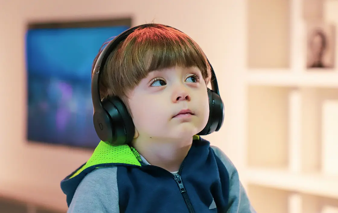 Junge mit braunem Haar, der große schwarze Kopfhörer trägt und mit neutralem Blick nach oben schaut.