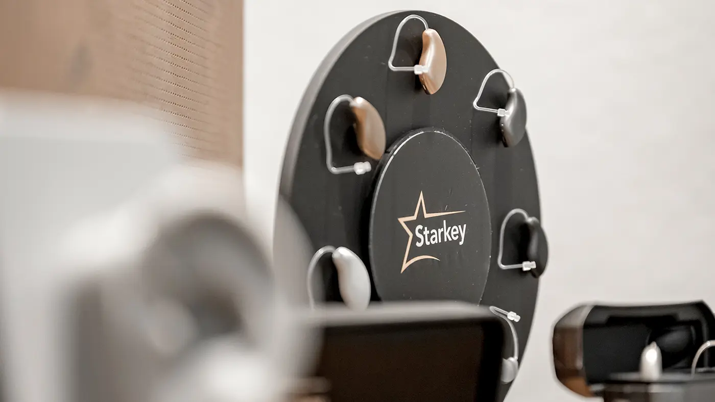 Ein schwarzer, runder Hörsystem-Halter mit mehreren Hörsystemen vor einer weißen Wand.