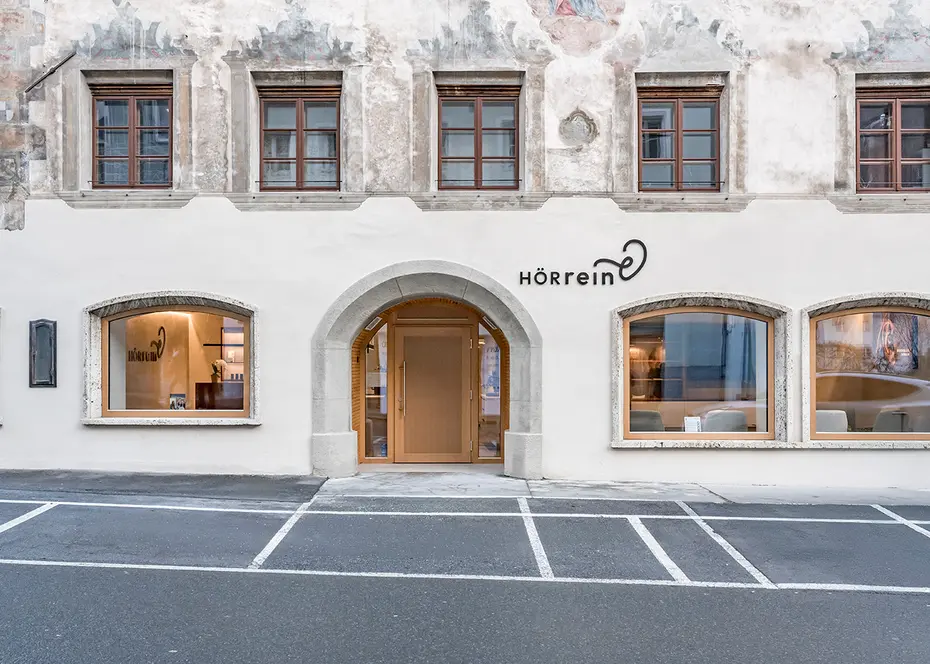 Gebäude mit Rundbogeneingang, großen Fenstern und dekorativer Fassade mit markierten Parkplätzen auf der Vorderseite.