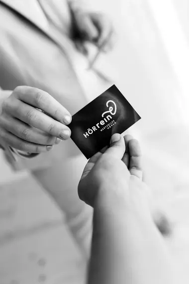 Schwarz-Weiß Foto von der Geschäftsführerin des Unternehmens, wie sie ihre Visitenkarte einer anderen Person übergibt.