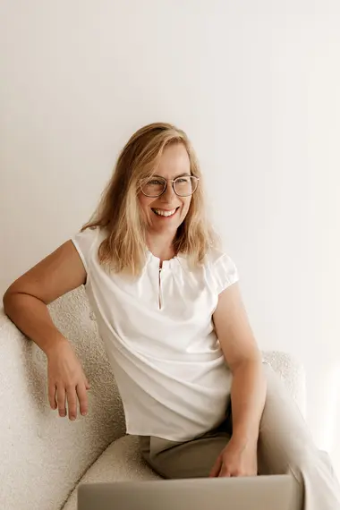 Die Geschäftsführerin sitzt lächelnd mit dem Laptop auf dem Sofa.