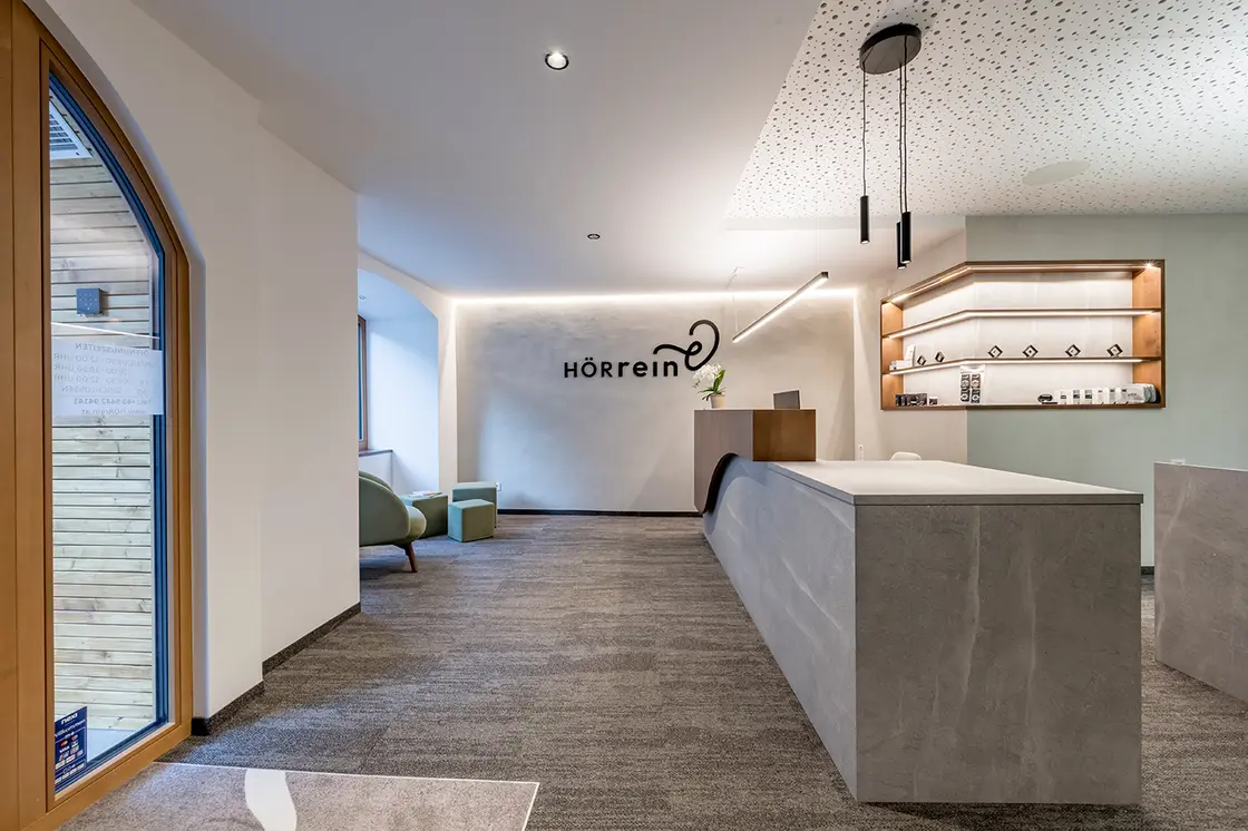 Moderner Empfangsbereich mit Betonschreibtisch, dekorativer Decke, großem Fenster und minimalistischem Dekor.