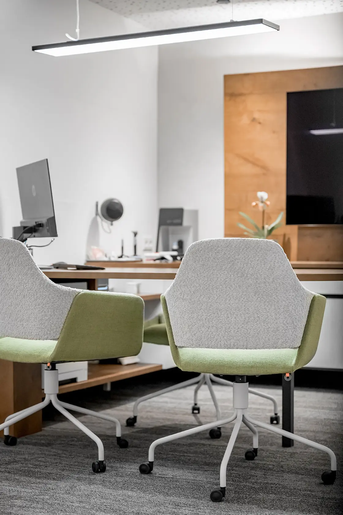 Zwei moderne Bürostühle stehen vor einem Schreibtisch mit Computern und Dekoration in einem modernen, gut beleuchteten Arbeitsbereich.