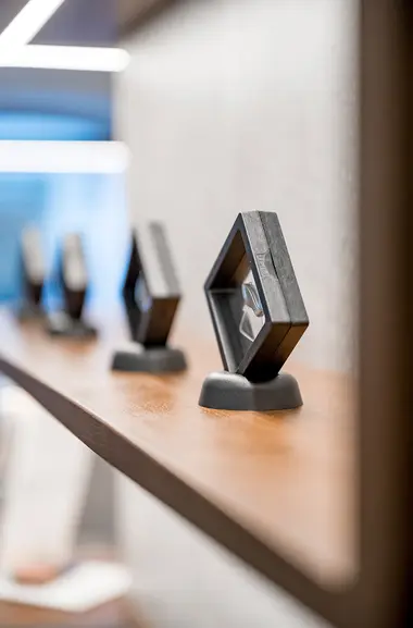 Eine Reihe moderner, geometrischer schwarzer Rahmen, in denen Hörsysteme sind, auf einem Holzregal mit unscharfem Hintergrund.