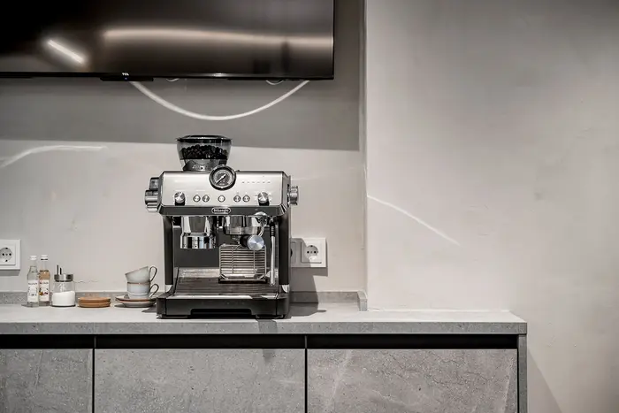 Eine moderne Espressomaschine steht auf einer grauen Arbeitsplatte vor einer hellen Wand.