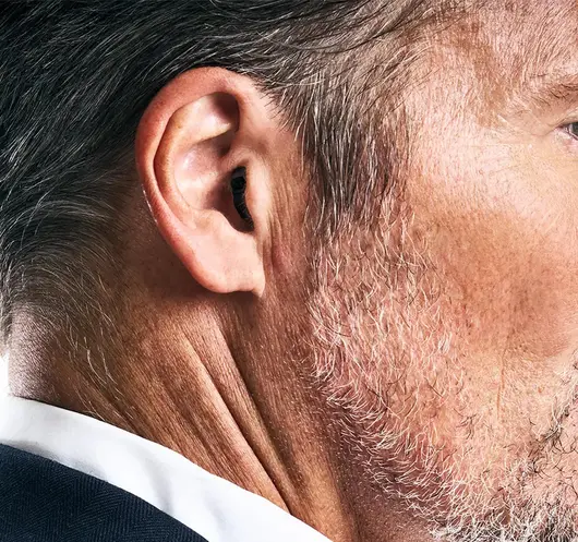 Nahaufnahme von dem Ohr eines Mannes. Er trägt ein Im-Ohr-Hörgerät, welches kaum zu sehen ist.