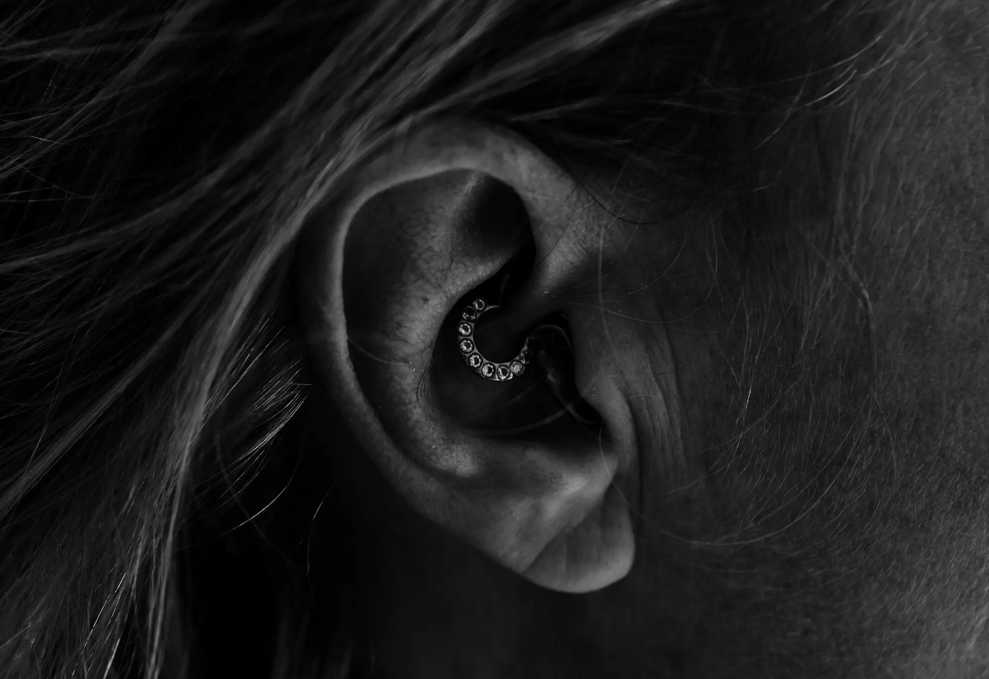 Nahaufnahme des Ohrs einer Person mit einem mit Edelsteinen besetzten Ohrring, aufgenommen in Schwarz-Weiß von Hörakustiker Landeck.