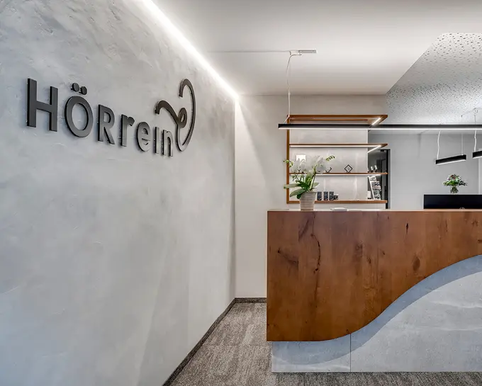 Moderner Empfangsbereich mit Rezeptionstisch und dem HÖRrein Logo an einer weißen Wand.