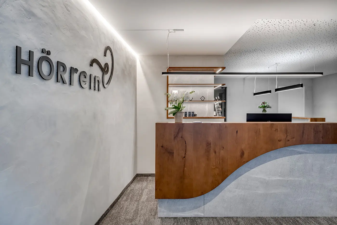 Moderner Empfangsbereich mit Rezeptionstisch und dem HÖRrein Logo an einer weißen Wand.