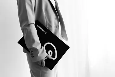 Person im Anzug, die eine schwarze Mappe mit dem Hörrein Logo in der Hand hält und an einem hellen Fenster steht.